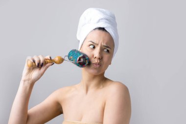 Kafasında havlu olan esmer, gri arka planda izole edilmiş yüz masajı için silindir kullanıyor.