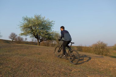 Şortlu ve formalı bisikletçi, modern karbon kuyruklu motorsikletli. Uçurumun kenarında, yeşil bahar ormanlarının arka planında duran bir hava süspansiyon çatalı var.