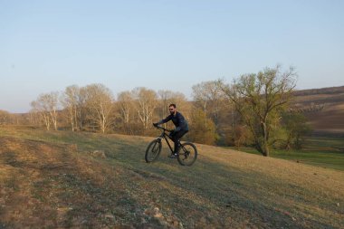 Şortlu ve formalı bisikletçi, modern karbon kuyruklu motorsikletli. Uçurumun kenarında, yeşil bahar ormanlarının arka planında duran bir hava süspansiyon çatalı var.