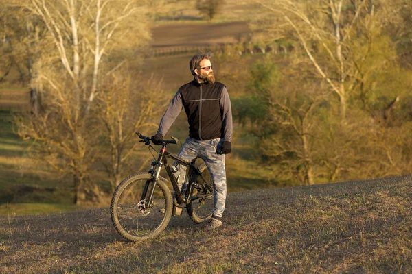 現代のマウンテンバイクで残酷な髭の男をスポーツ 春の緑の丘の上のサイクリスト — ストック写真