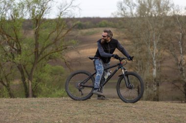 Modern dağ bisikletindeki vahşi sakallı adam. Baharda yeşil tepelerde bisikletçi.