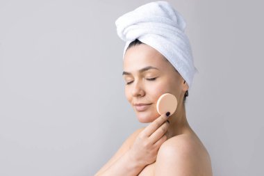 Kafasında beyaz havluyla güzel bir kadın portresi ve pembe bir kalbe bakan bir vücut için sünger. Cilt temizleme eko organik kozmetik rahatlama konsepti.