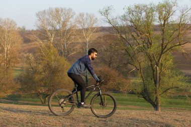 Şortlu ve formalı bisikletçi, modern karbon kuyruklu motorsikletli. Uçurumun kenarında, yeşil bahar ormanlarının arka planında duran bir hava süspansiyon çatalı var.