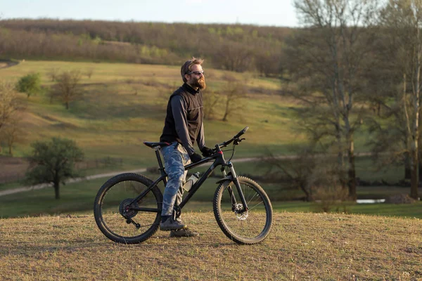 現代のマウンテンバイクで残酷な髭の男をスポーツ 春の緑の丘の上のサイクリスト — ストック写真