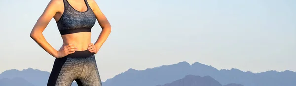 A thin athletic girl takes a break between classes on the background of mountains in the early morning, enjoys silence and freedom.