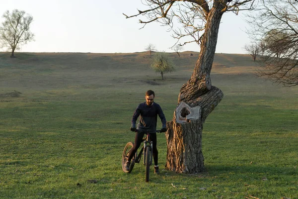 Cyclist in shorts and jersey on a modern carbon hardtail bike with an air suspension fork standing on a cliff against the background of fresh green spring forest