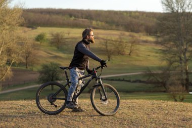 Modern dağ bisikletindeki vahşi sakallı adam. Baharda yeşil tepelerde bisikletçi.