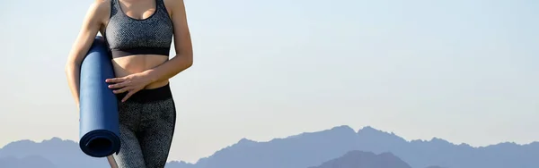 A thin athletic girl takes a break between classes on the background of mountains in the early morning, enjoys silence and freedom.