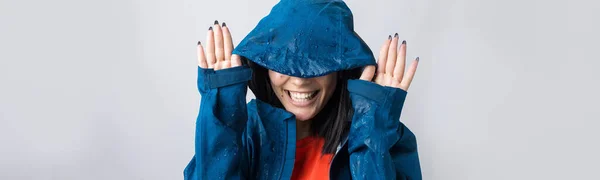笑顔の女の子の肖像画で青レインコートに身を包んだ滴でフードととともに灰色の背景でスタジオ — ストック写真