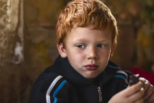 Portrait homeless unclean kid. Hungry child with big clear eyes eating. Red-haired little boy. Close-Up. Concept of social problems. Life on the street — Stock Photo, Image