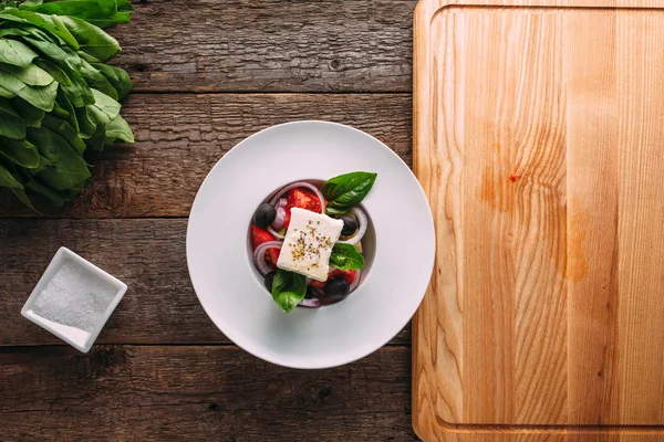 Ahşap bir masa üzerinde beyaz bir tabak içinde klasik Yunan salatası