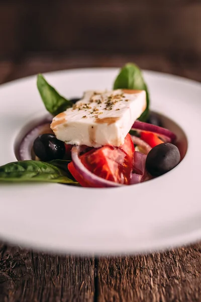 Ahşap bir masa üzerinde beyaz bir tabak içinde klasik Yunan salatası