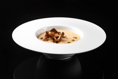 Siyah arka planda beyaz tabakta mantarlı krema çorbası.