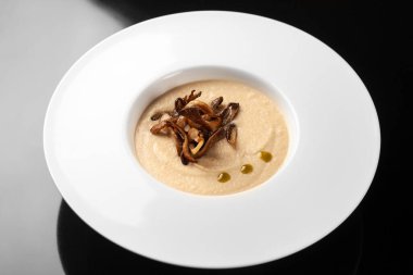 Siyah arka planda beyaz tabakta mantarlı krema çorbası.