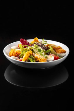 Siyah arka planda beyaz tabakta tavuklu Sezar salatası.