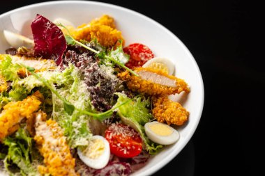 Siyah arka planda beyaz tabakta tavuklu Sezar salatası.