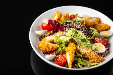 Siyah arka planda beyaz tabakta tavuklu Sezar salatası.