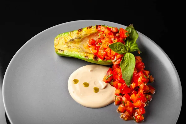 Siyah arka planda tahini soslu ızgara avokado salatası.