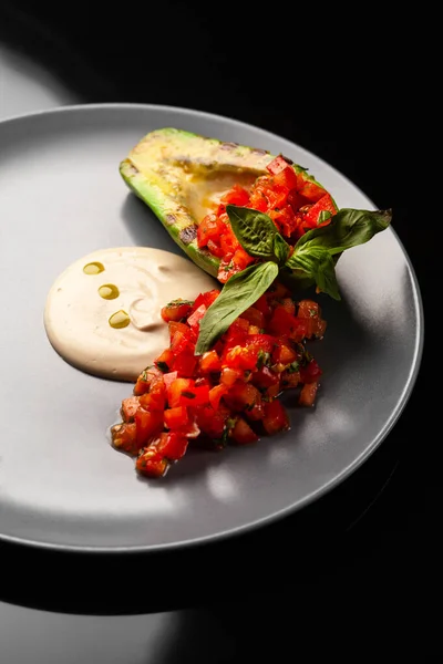 Siyah arka planda tahini soslu ızgara avokado salatası.