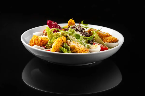 Siyah arka planda beyaz tabakta tavuklu Sezar salatası.