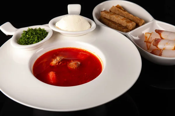 Siyah arka planda beyaz bir tabakta domuz pastırması ve kızarmış ekmekle Ukrayna Borsch 'u.