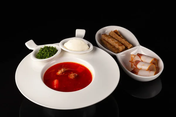 Siyah arka planda beyaz bir tabakta domuz pastırması ve kızarmış ekmekle Ukrayna Borsch 'u.