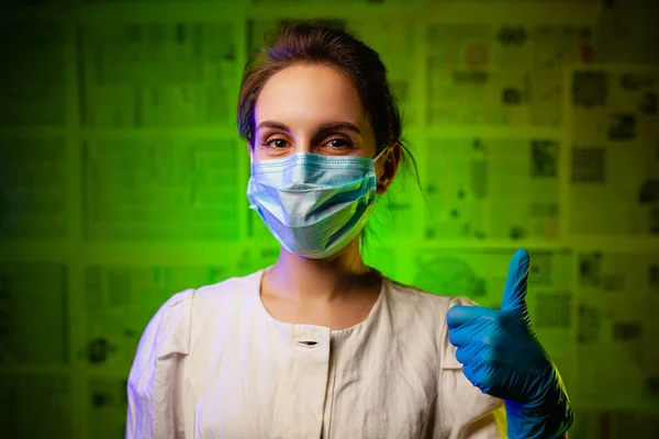 Maskeli ve eldivenli mutlu doktor her şeyin yolunda olduğunu gösteriyor. Tıbbi maske takan ve yeşil arka planda lastik eldiven takan bir tıp çalışanı. Koronavirüs salgınına karşı zafer