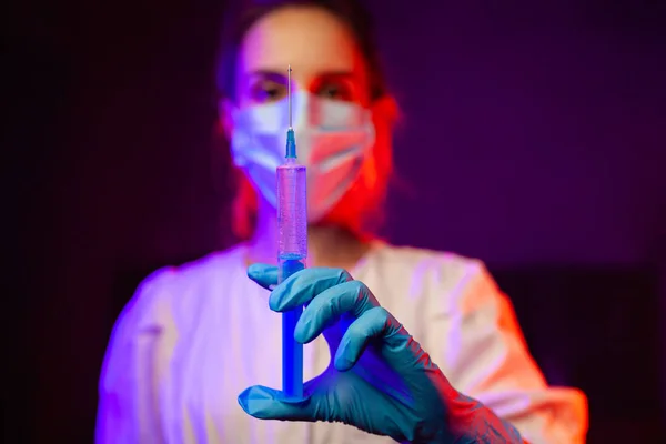 Elinde şırıngayla tıbbi maske takan bir doktor. Karanlık bir odada elinde şırıngayla kırmızı ve mavi ışığı olan genç bir sağlıkçı kız. Coronavrius salgını sırasında sağlık görevlisi.