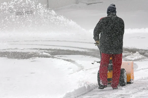 Зимой человек убирает снег. Очистка снега с помощью снежной мельницы — стоковое фото