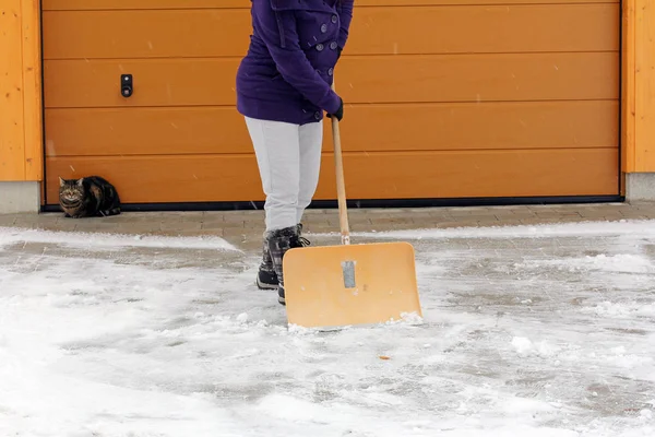 Снегоуборка зимой - женщина убирает снег перед гаражом — стоковое фото