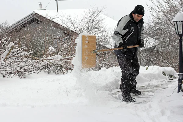 Um homem no inverno limpa a neve de um caminho — Fotografia de Stock