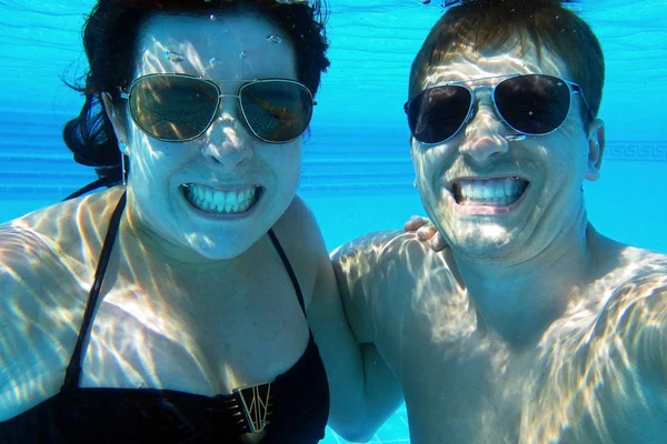 An underwater photo of a laughing couple. A laughing woman and a laughing man in the pool — Stock Photo, Image