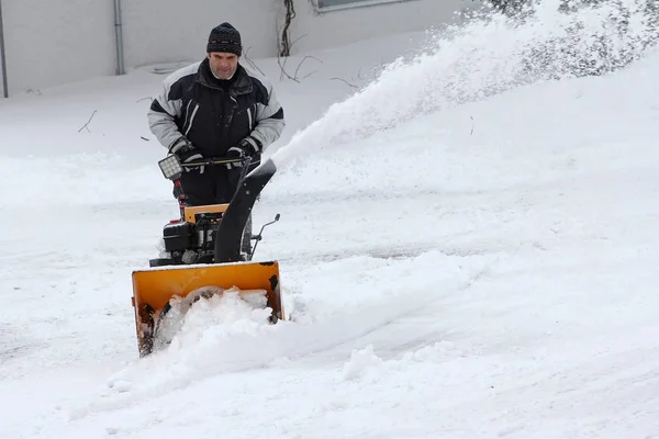 Um homem limpa a neve no inverno. Limpeza de neve com o moinho de neve — Fotografia de Stock