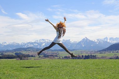 Genç bir kadın mutlu havaya atlar. Bir hava atlamak bahar dağların önünde doğada