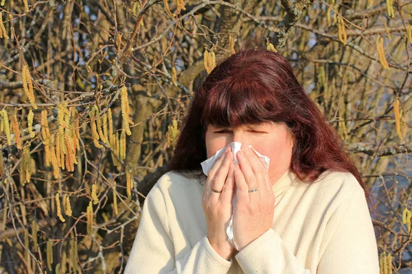 A woman has hay fever. Hay fever begins in spring. A woman has a cold and is blowing into a handkerchief