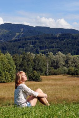 Bavyera bir çayır üzerinde oturan genç bir sarışın kadın rahat