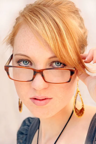 A pretty young woman looks interested and curious about the rim of the glasses