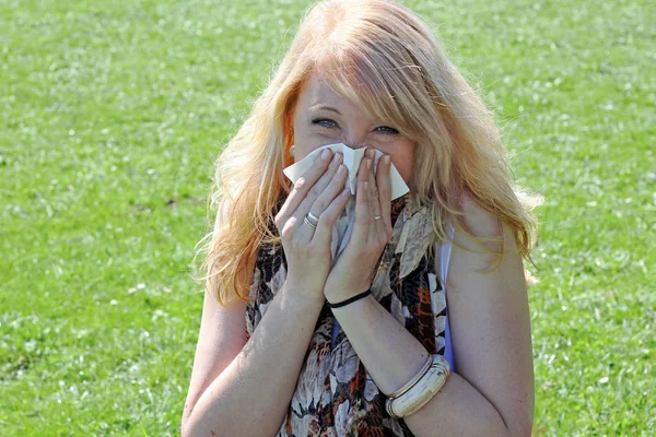 A young woman has hay fever. Hay fever begins in spring. A woman has a cold and is blowing into a handkerchief
