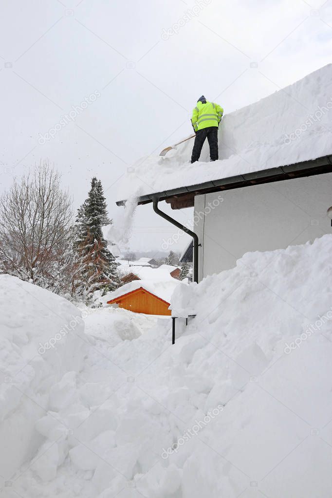 A man shovels dangerously heavy snow from a house roof