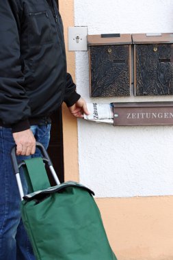 Bir gazete dağıtıcısı günlük gazeteyi getirir ve bir posta kutusuna koyar.