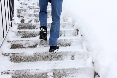 In winter it is dangerous to walk up a snow-covered staircase. A man walks up a staircase in winter clipart