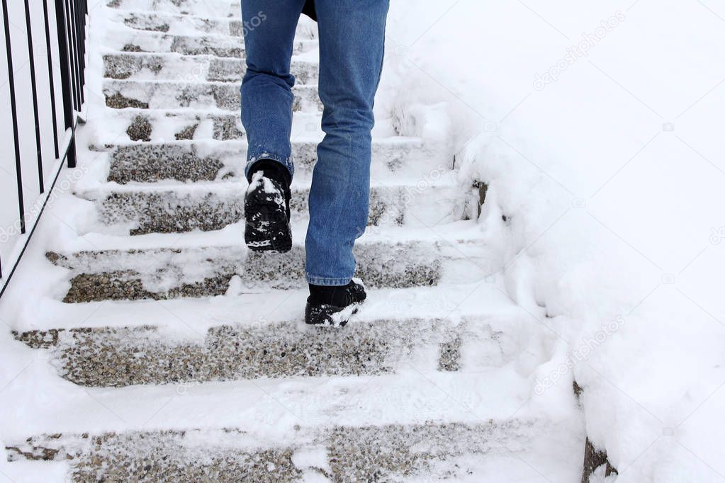 In winter it is dangerous to walk up a snow-covered staircase. A man walks up a staircase in winter
