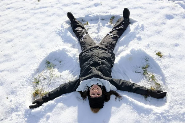 若い女性が冬の雪の中で雪の天使を作る — ストック写真