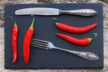 Kırmızı biberler ve eski gümüş çatal bıçak takımı siyah bir levhada