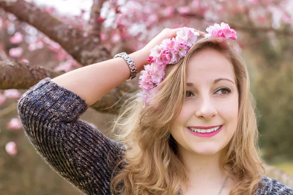 Glad ung kvinna med en krans på huvudet i den blommande våren trädgården — Stockfoto