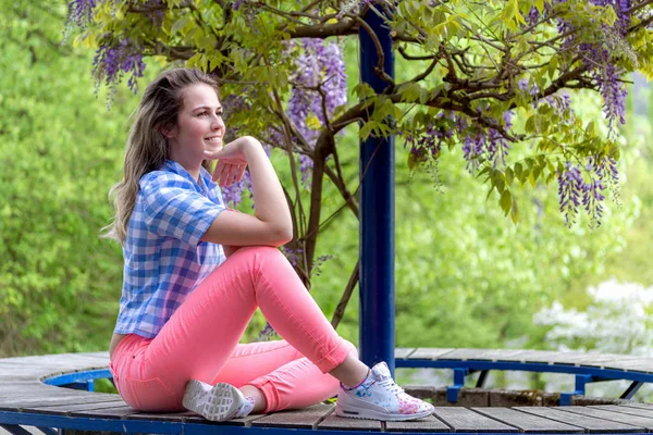 Mujer joven posando al aire libre sobre un fondo de glicina floreciente — Foto de Stock
