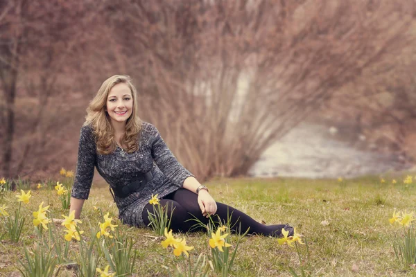 Ung kvinna sitter i en park med blommande påskliljor — Stockfoto
