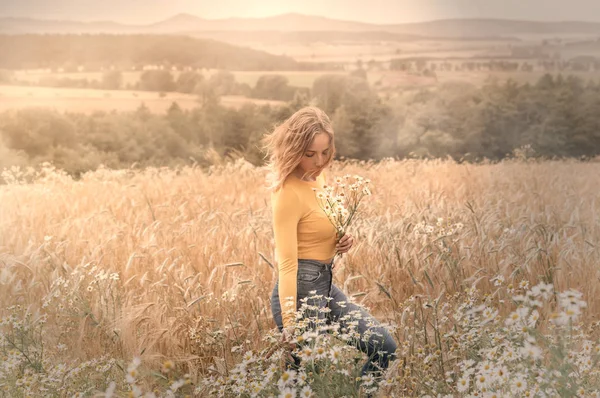 Junge Frau in einem Weizenfeld mit Gänseblümchen in den Händen — Stockfoto