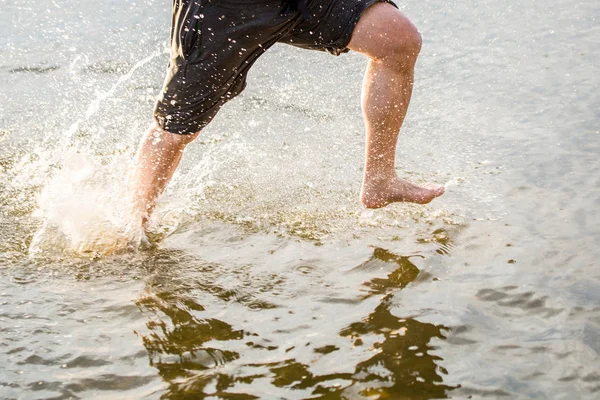 Un homme courant le long d'une plage et éclaboussant l'eau — Photo