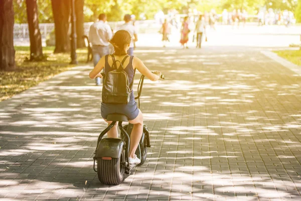 O femeie tânără de echitatie zero emisii eco biciclete scuter electric într-un parc de oraș . — Fotografie, imagine de stoc